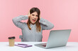 © khosrork - Exhausted irritated business woman covering ears with hands sitting at workplace with laptop, annoyed by noisy sound, tired of office chatter. Indoor studio shot isolated on pink background