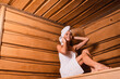 © LIGHTFIELD STUDIOS - Low angle view of cheerful woman in white towels sitting in sauna