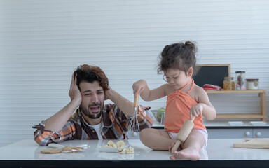 Wall Mural - Caucasian father with beard shocking when he looking at his little daughter holding whisk and rolling pin to crush mash cookies they made together in the kitchen at home