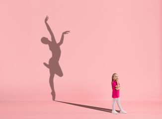 Childhood and dream about big and famous future. Conceptual image with girl and drawned shadow of female ballet dancer on coral pink background. Childhood, dreams, imagination, education concept.