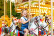 © Any Grant - happy baby girl rides a carousel on a horse in an amusement Park in summer