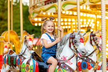 Happy Baby Girl Rides A Carousel On A Horse In An Amusement Park In Summer
