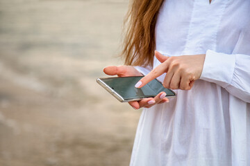 Woman use mobile phone to search in internet or check app outside with copy space. Closeup female hands with smartphone rest at sea water background. Woman text message in traveling