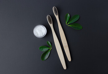 two wooden bamboo eco friendly toothbrushes, dentifrice and green leaves on black background. 