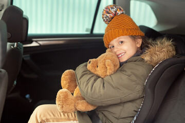 Wall Mural - Cheerful cute little girl in warm winterwear holding and embracing teddybear