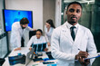 © Ivan - African American doctor looking at the camera. behind him, doctors of different nationalities are talking, sitting at the table in the first-aid post.