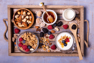 Wall Mural - On the wooden tray, tasty breakfast with yogurt, cereals, dried fruit, raspberries, blueberries and blackberries, bowl with forest honey. view from top