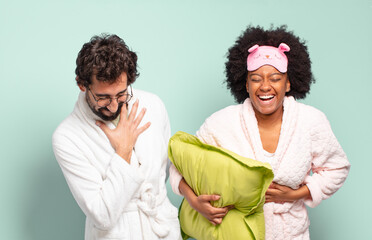 Wall Mural - multiracial couple of friends laughing out loud at some hilarious joke, feeling happy and cheerful, having fun. pajamas and home concept