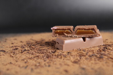 Wall Mural - A cut of chocolate stuffed with caramel chocolate bar lies on the cocoa on a black background with place for text and a copy of the day of chocolate