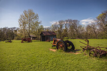 Old Rusty Farm Equipment And Tractor By A Barn
