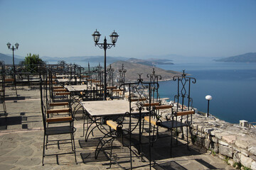 Empty outdoor cafe with forged furniture overlooking the city by the sea, Albania