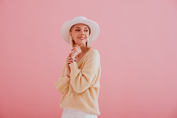 Happy smiling woman wearing trendy yellow sweater, white hat posing on pink background. Spring fashion conception. Copy, empty space for text