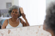 © Wavebreak Media - Thoughtful african american senior woman brushing her hair while looking in the mirror at home