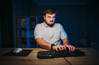 © bodnarphoto - Emotional bearded freelancer man angrily typing on the keyboard at night at home, looking at the camera with an evil face. Deadline.
