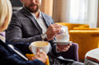 © Roman - conversation between business people dressed in suits sitting with coffee in hotel restaurant during business trip, have a nice talk. cropped man and woman holding cups