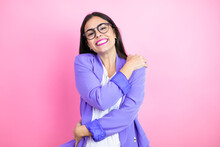Young Business Woman Wearing Purple Jacket Over Pink Background Hugging Oneself Happy And Positive, Smiling Confident