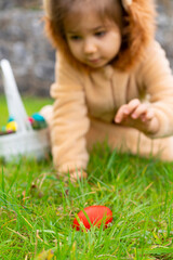 Cute cheerful child in a lion costume looking for and gathering easter eggs in the backyard lawn or park. Easter eggs hunt on spring meadow. Blurred kid's silhouettes with basket. 