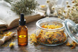 Dropper bottle of calendula infusion or oil, jar of dried marigold flowers, old recipes book and chamomile bunch on background. Alternative medicine.