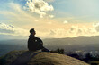 young boy sitting on top of a mountain looking to the horizon. enterprising man sitting on a rock with background sunset landscape. dark teenager with Latino features on a mountain