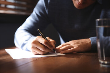 Man writing letter at wooden table indoors, closeup