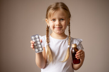 A little girl with pigtails smiles and holds a bottle of medicine and pills in her hands, plays a children's doctor. Health concept, pediatrician