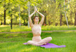© elenbessonova - Pretty beautiful woman doing yoga exercises in the park. Fit girl teacher stretching outdoors on summer day. Sporty young woman doing pilates practice. She looks very calm. Healthy lifestyle concept.