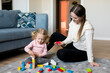 © tgordievskaya - Mother and daughter playing wooden cubes on the floor of the living room at home. Activities with children inside, early childhood development