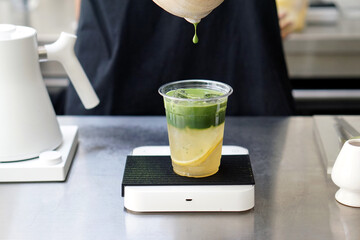 Iced matcha lemon soda - Pouring green tea into a glass of honey lemon soda on the table.