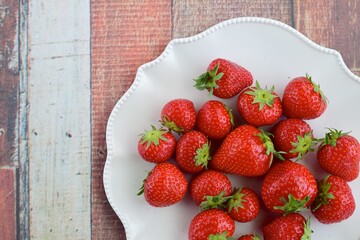 Fresh organic strawberry on white plate on wooden background. Flat lay