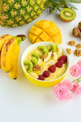 Mango banana pineapple smoothie bowl topped with raspberry, kiwi, walnut and coconut chips