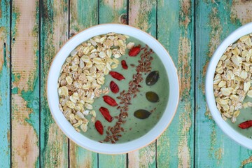 Nutritious green smoothie bowl with goji berries, oats, pumpkin seeds, sunflower seeds and flax seeds on green wood background. Top view
