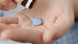 Two big blue diamond-shaped pills labeled 100 fall into palm of hand from pill bottle. Close-up, front view, center composition