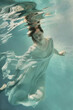 A girl in an airy light dress swims underwater as if flying in zero gravity