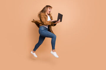 Wall Mural - Full body profile side photo of nice amazed blonde woman hold computer jump up run empty space isolated on beige color background