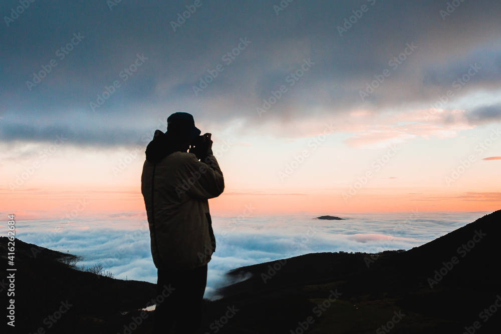 Silhouette of photographer on top of mountain peak over clouds ...