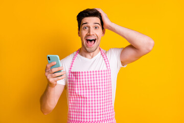 Sticker - Photo portrait of astonished man touching head screaming holding phone in one hand isolated on vivid yellow colored background