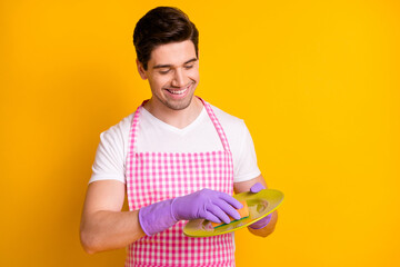 Sticker - Photo portrait of guy in purple rubber gloves washing plate with sponge isolated on vivid yellow colored background