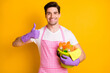© deagreez - Photo of young happy positive handsome man showing thumb-up hold bucket full of detergent isolated on yellow color background