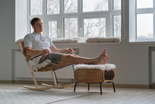 Young Man Relaxing On Cozy Rocking-chair In Light Room. Joy Of Life. Total Relaxation.