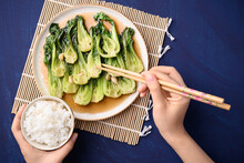 Stir Fried Bok Choy With Soy Sauce On Plate Eating With Cooked Rice By Using Chopsticks On Blue Background, Asian Vegan Food, Top View