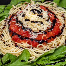 Spaghetti Pasta With Red Sauce, Arugula, Parmesan Cheese And Balsamic Vinegar On Black Plate With White Marble Background