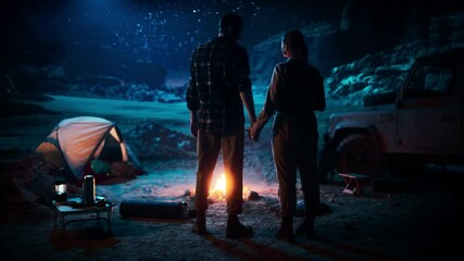 Wall Mural - Happy Couple Camping in the Canyon at Night, Standing by Campfire, Holding Hands Lovingly and Romantically Watching Star Sky. Two Traveling people on a Nature Inspirational Vacation Trip, Journey 