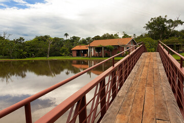 Bridge on lake, with house in the background, showing sky, trees and farm