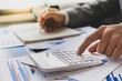 © crizzystudio - Asian male finance staff is calculating the investment results to deliver a report to his supervisor at the meeting. On the table in the office, the concept of calculating investment results