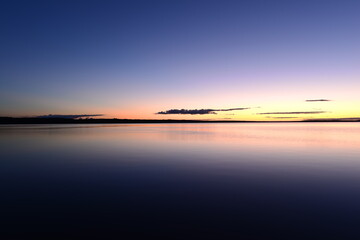 Wall Mural - Blue sky in the orange twilight glow on horizon over calm azure water lake