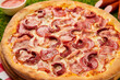 © bondvit - Traditional italian Pizza with salami, mozzarella, ham and bacon on green grass background