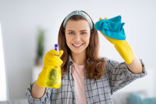Portrait Of Smiling Young Woman In Rubber Gloves Cleaning Glass With Spray Detergent, Indoors