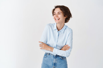 Candid young office woman in blue collar shirt, laughing and smiling happy, looking aside at empty space logo, standing on white background