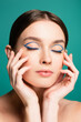charming woman with blue eyeliner in closed eyes posing with hands near face isolated on green