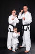 Portrait of happy young family in martial arts uniform standing over black background.